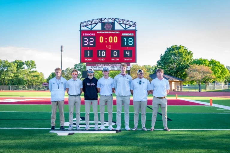Students standing in front of the digital scoreboard on Hardesty Football Field