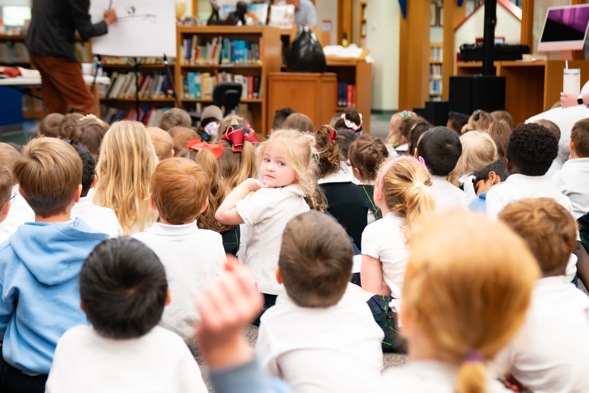 Group of Holland Hall Primary School students faced away from camera listening to a presentation. One student in the middle is turning toward camera.