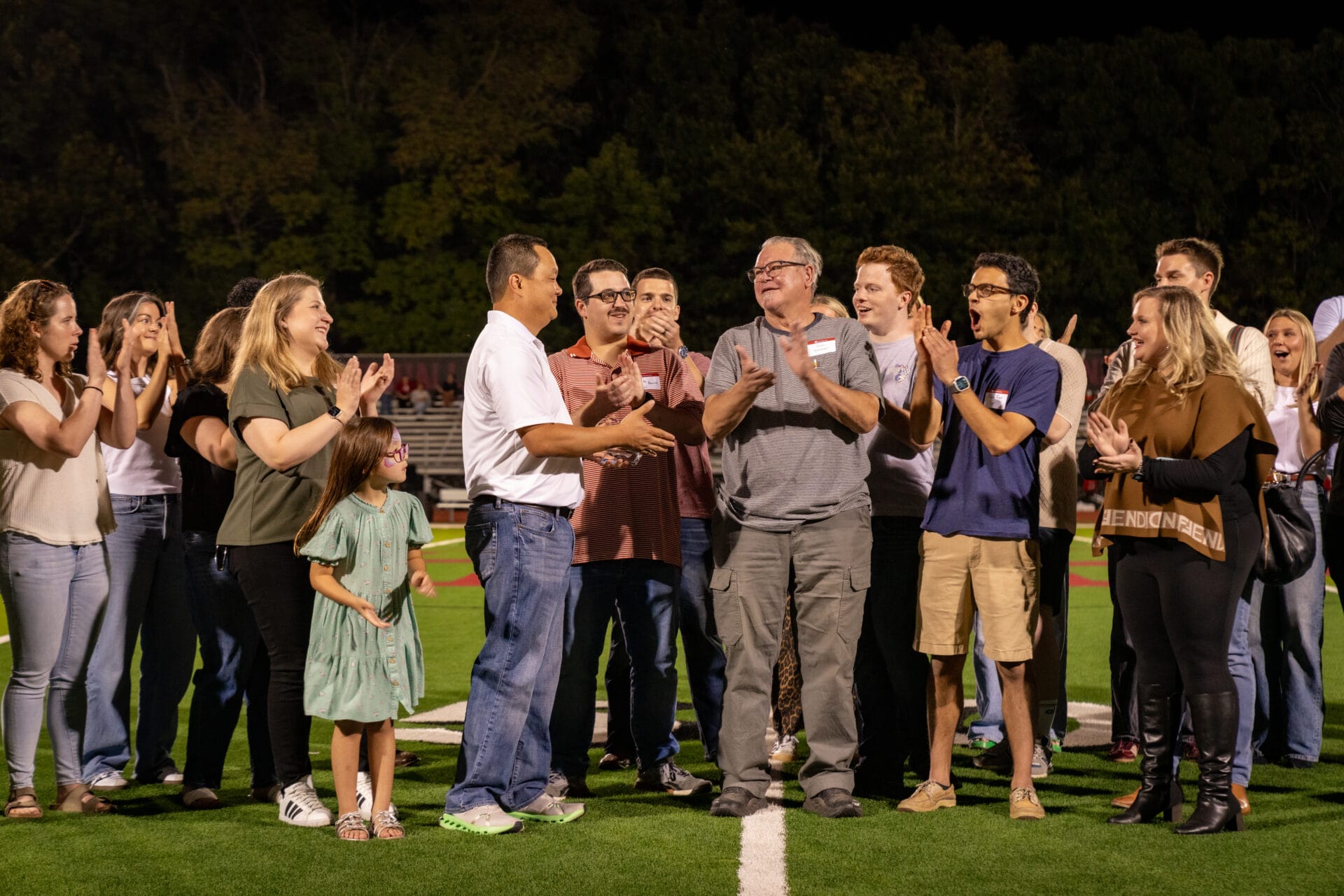 Former teacher Gary Sweeney is honored during halftime of the football game at Alumni Weekend. Sweeney is standing on the 50-yard line surrounded by former students.